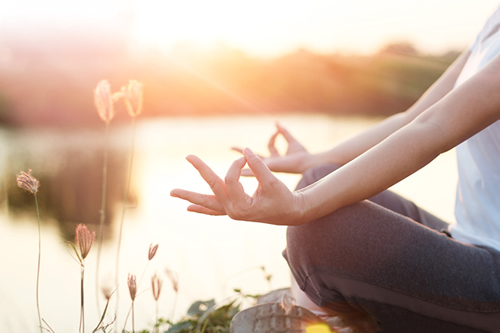 Frau macht Yoga im Abendlicht am Wasser